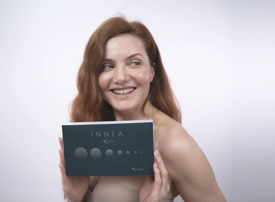 Smiling woman holding the INNEA Aqua product box, expressing joy and freshness associated with skin hydration treatments.