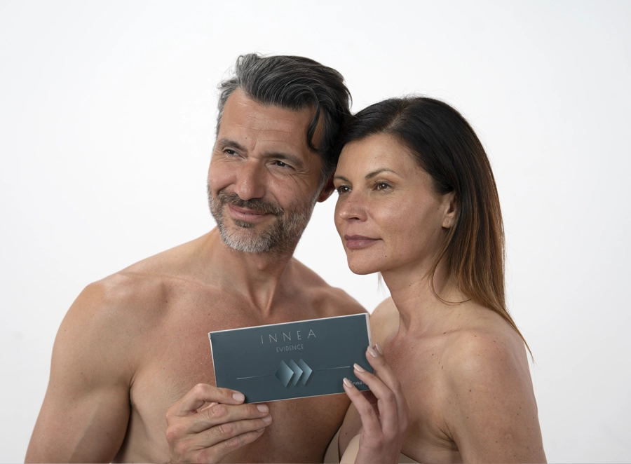 Smiling man and woman standing together holding the INNEA Evidence product box, representing shared confidence in aesthetic treatments.