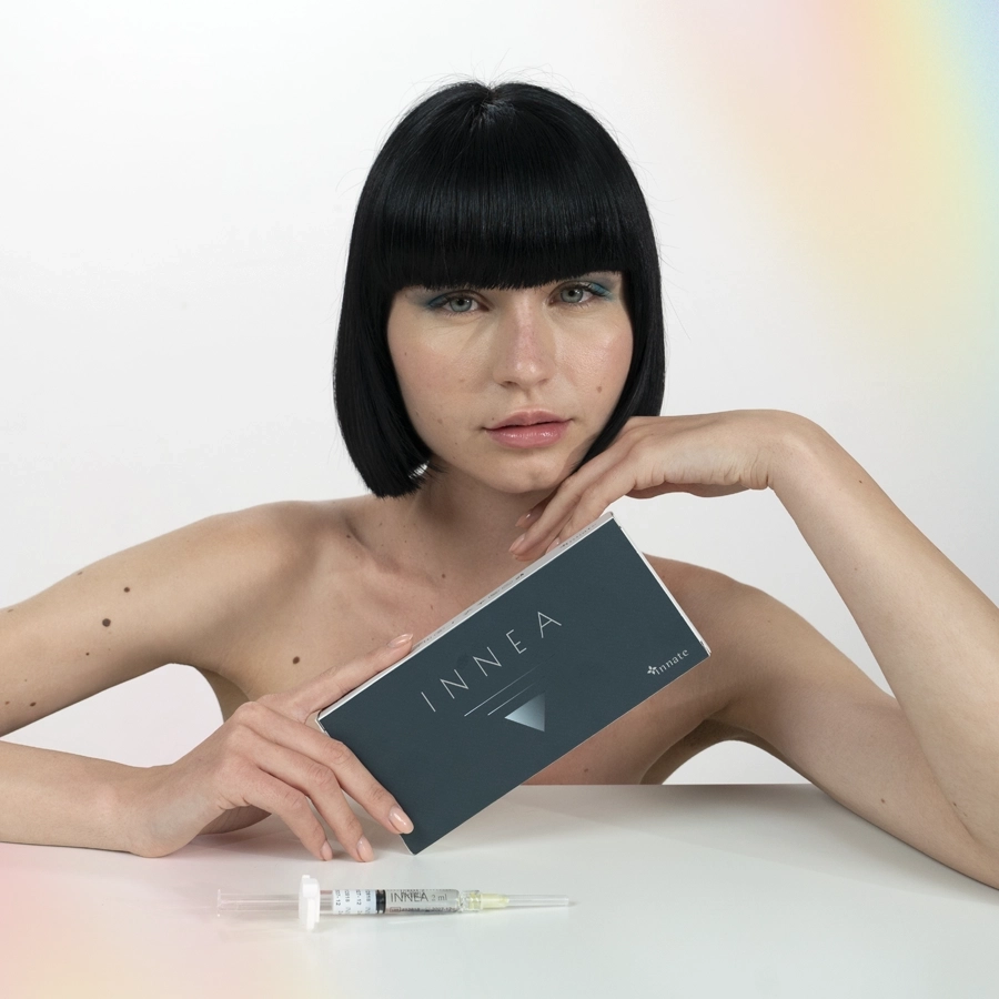 Woman with short black hair holding the INNEA Classic product box, with syringe in front, symbolizing essential care and aesthetic refinement.